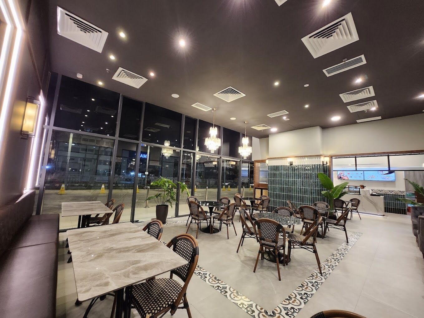 A restaurant with multiple tables and chairs, large windows, and ceiling lights.