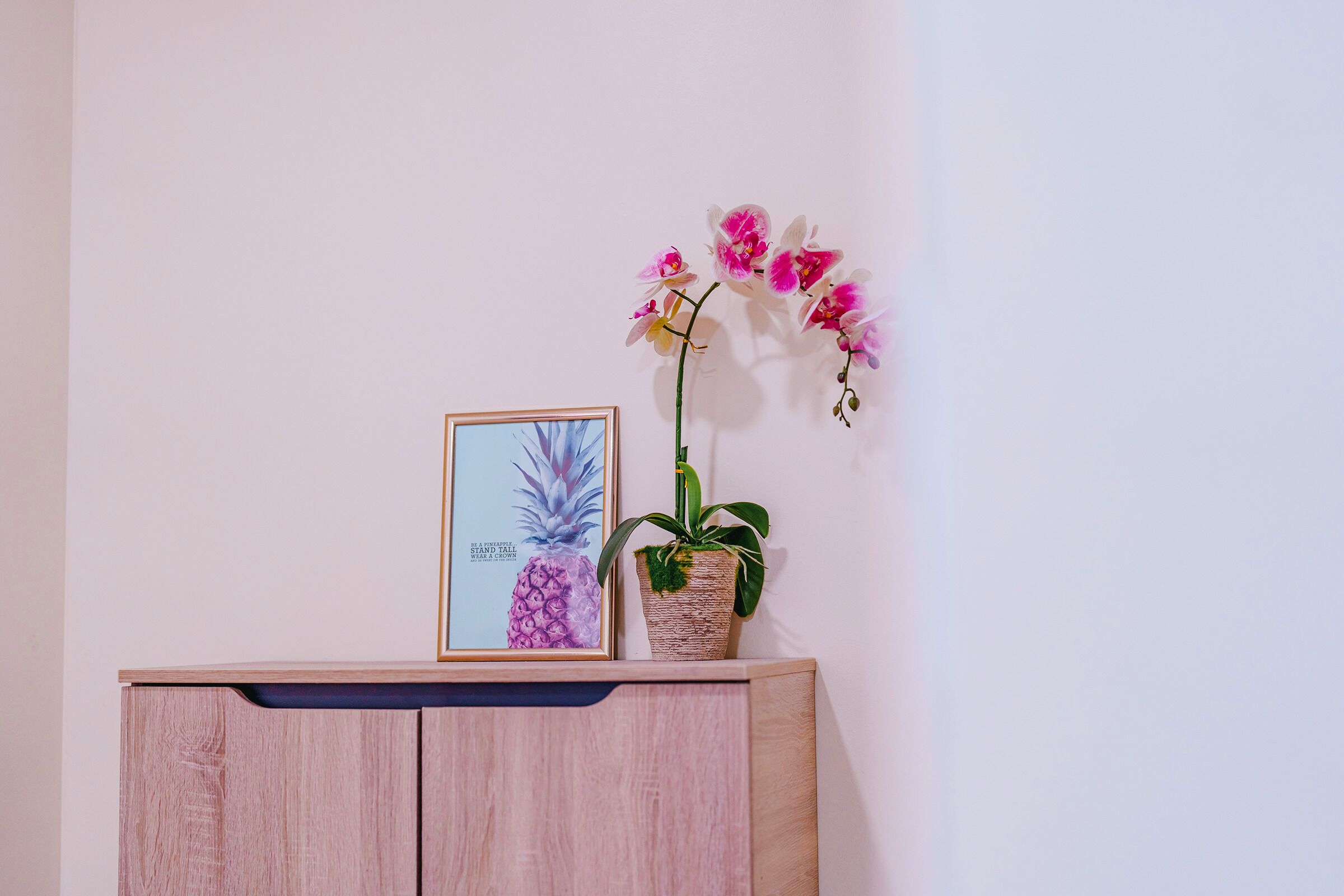 A wooden cabinet with a framed picture of a pineapple and a potted orchid.