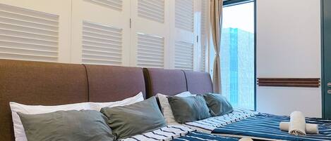 A hotel room with a large bed, multiple pillows, and a view of the city through the window.