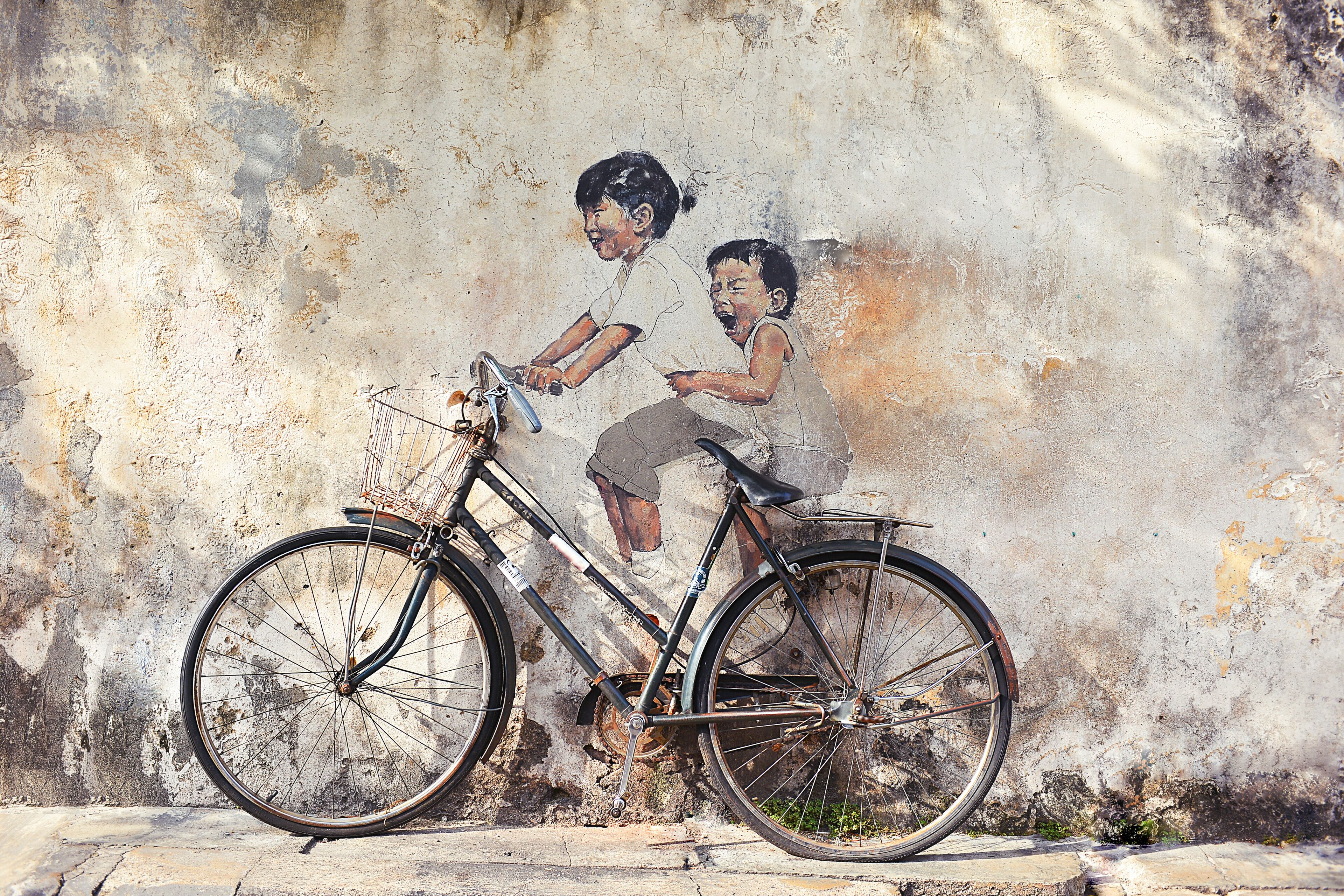 A bicycle with a basket, leaning against a textured wall.