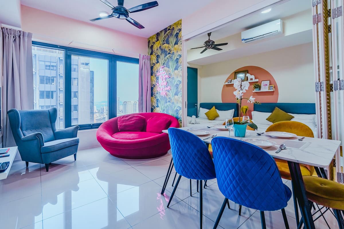 A modern living room with a blue armchair, a red sofa, and a dining area with blue chairs and a white table.