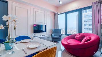 A modern living room with a dining area, a large window with a city view, a flat-screen TV, and a red bean bag chair.