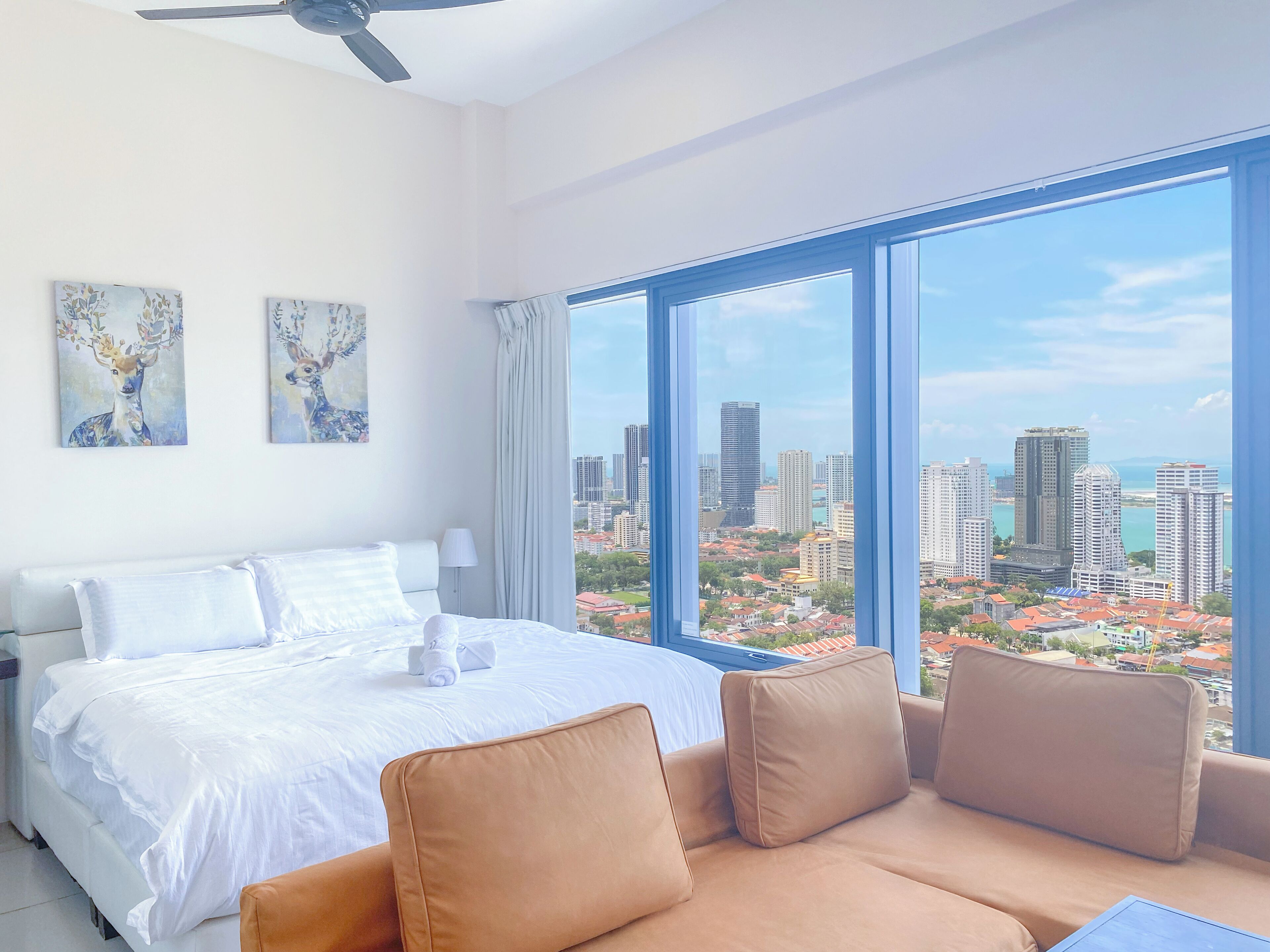 A hotel room with a large bed, a sofa, and a city view through large windows.