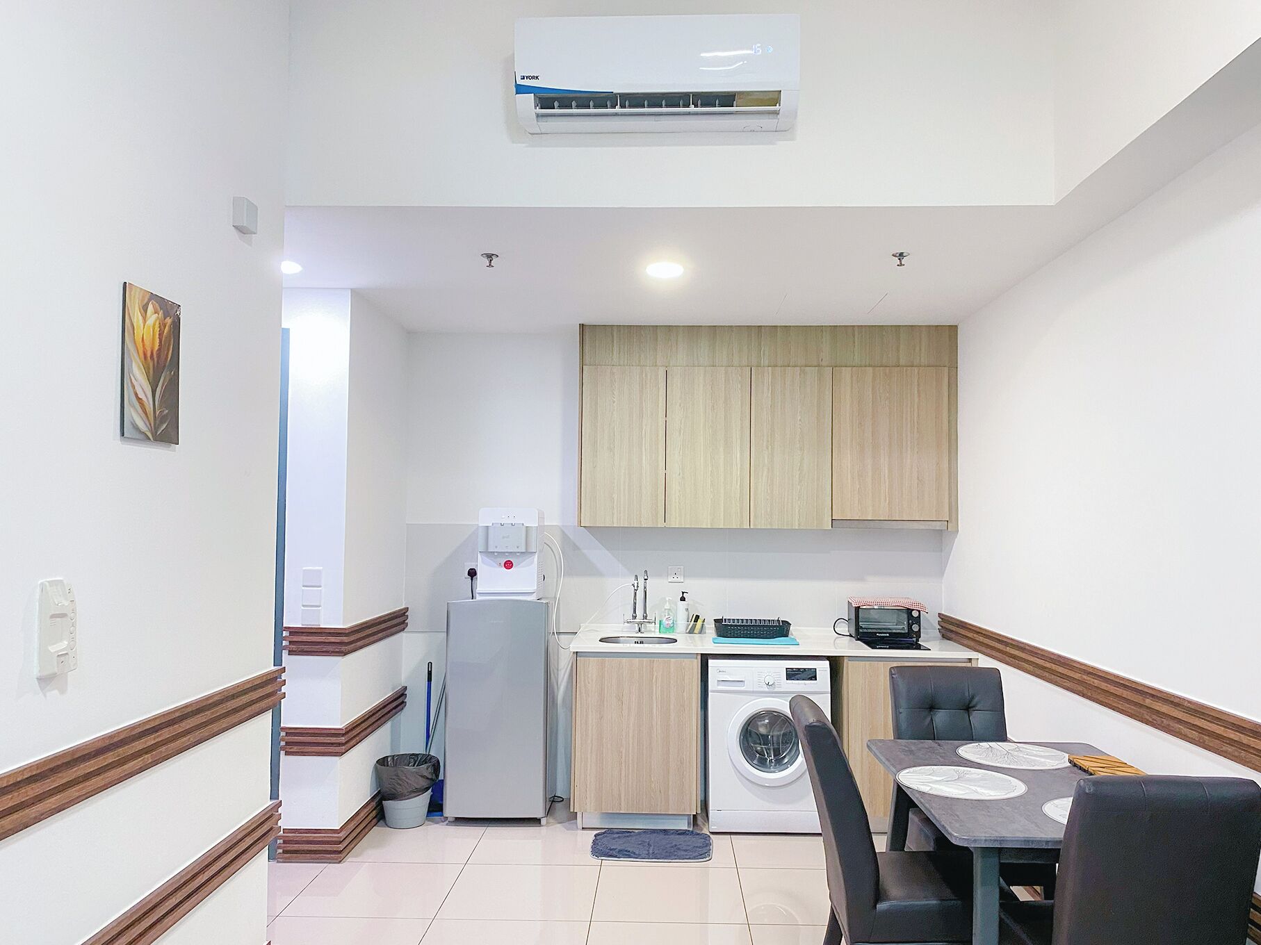 A compact kitchen with a washing machine, a coffee machine, and a small dining area with a table and chairs.