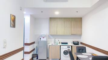 A compact kitchen with a washing machine, a coffee machine, and a small dining area with a table and chairs.