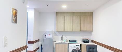 A compact kitchen with a washing machine, a coffee machine, and a small dining area with a table and chairs.
