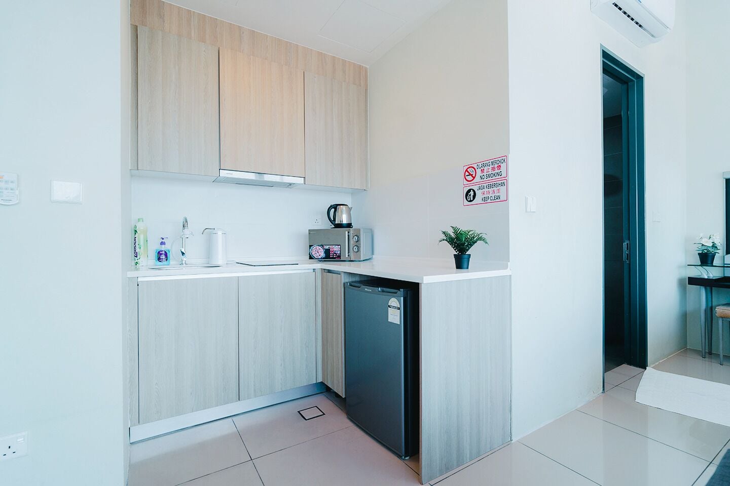 Una cocina moderna con armarios de madera, un microondas y un lavavajillas. Un letrero en la pared indica que no se permite fumar y mantener limpio.