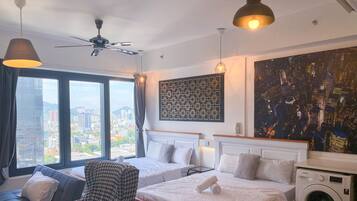 A hotel room with two beds, a sofa, a chair, a washing machine, and a cityscape view.