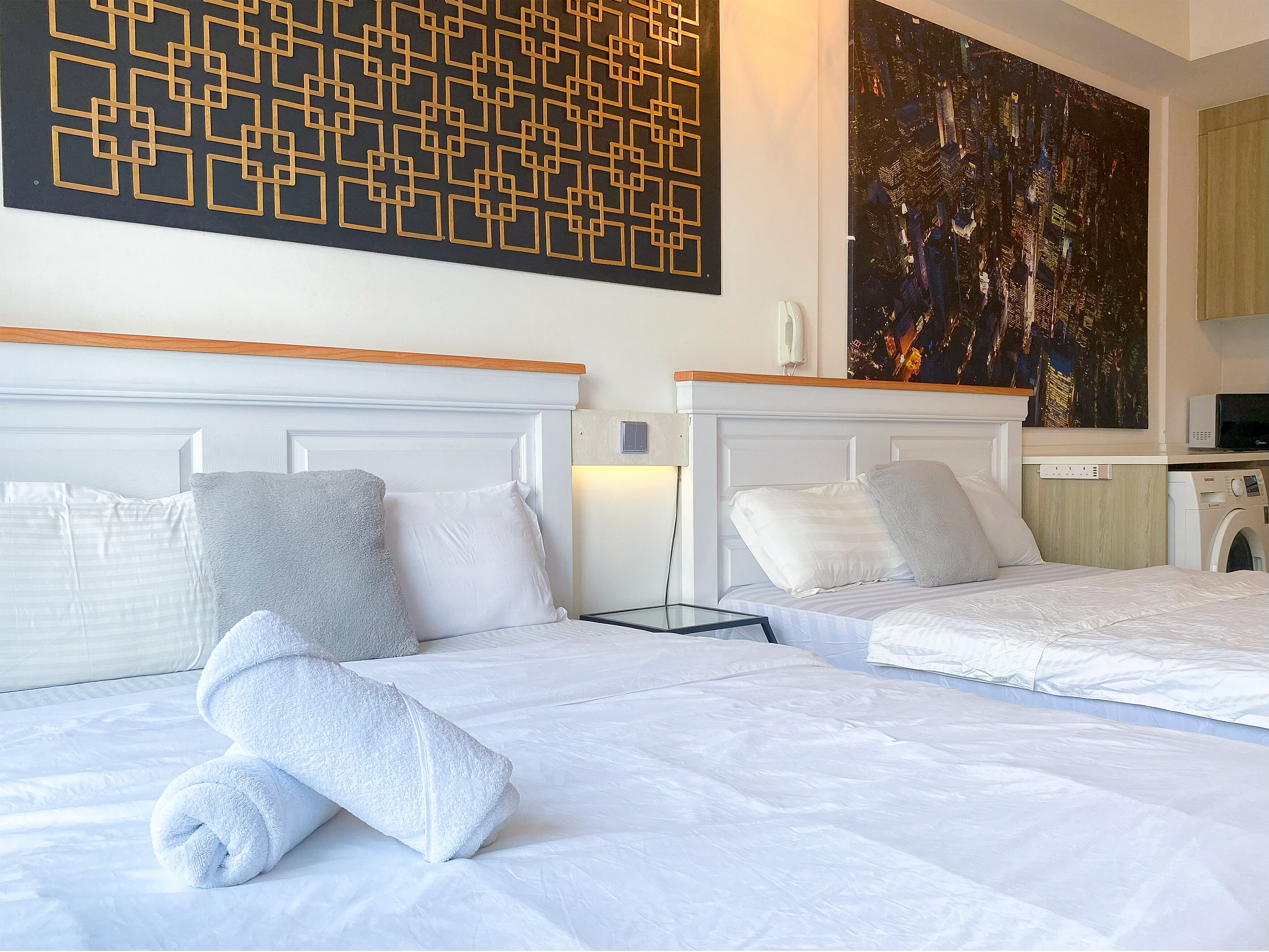 Hotelkamer met twee bedden, een groot abstract schilderij, een wasmachine en uitzicht op de stad 's nachts.