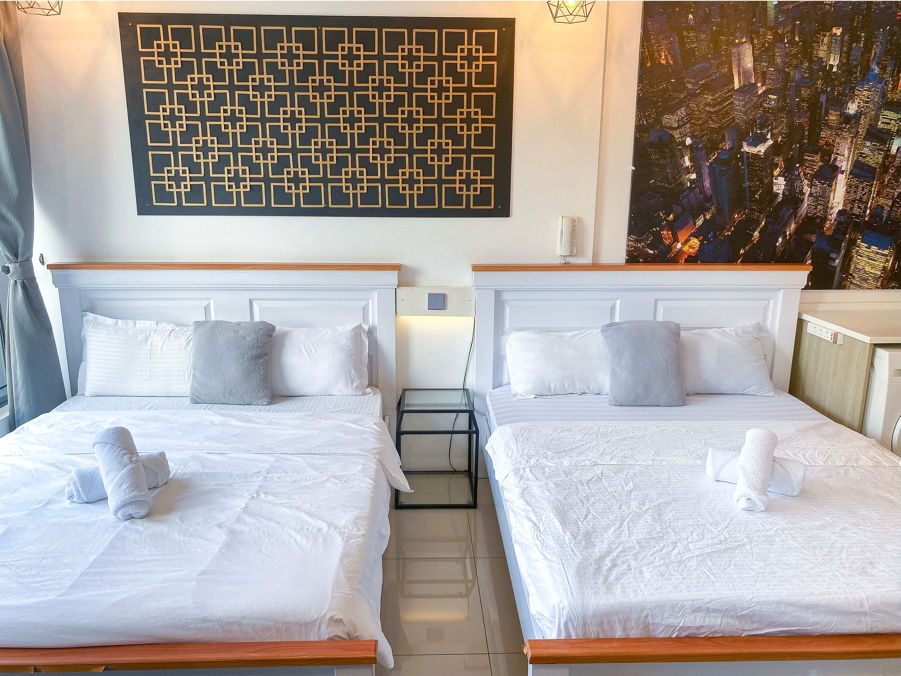 Ein Hotelzimmer mit zwei Betten, jeweils mit weißer Bettwäsche und Kissen, einem Nachttisch, einem Wandbild und Blick auf die Stadt.