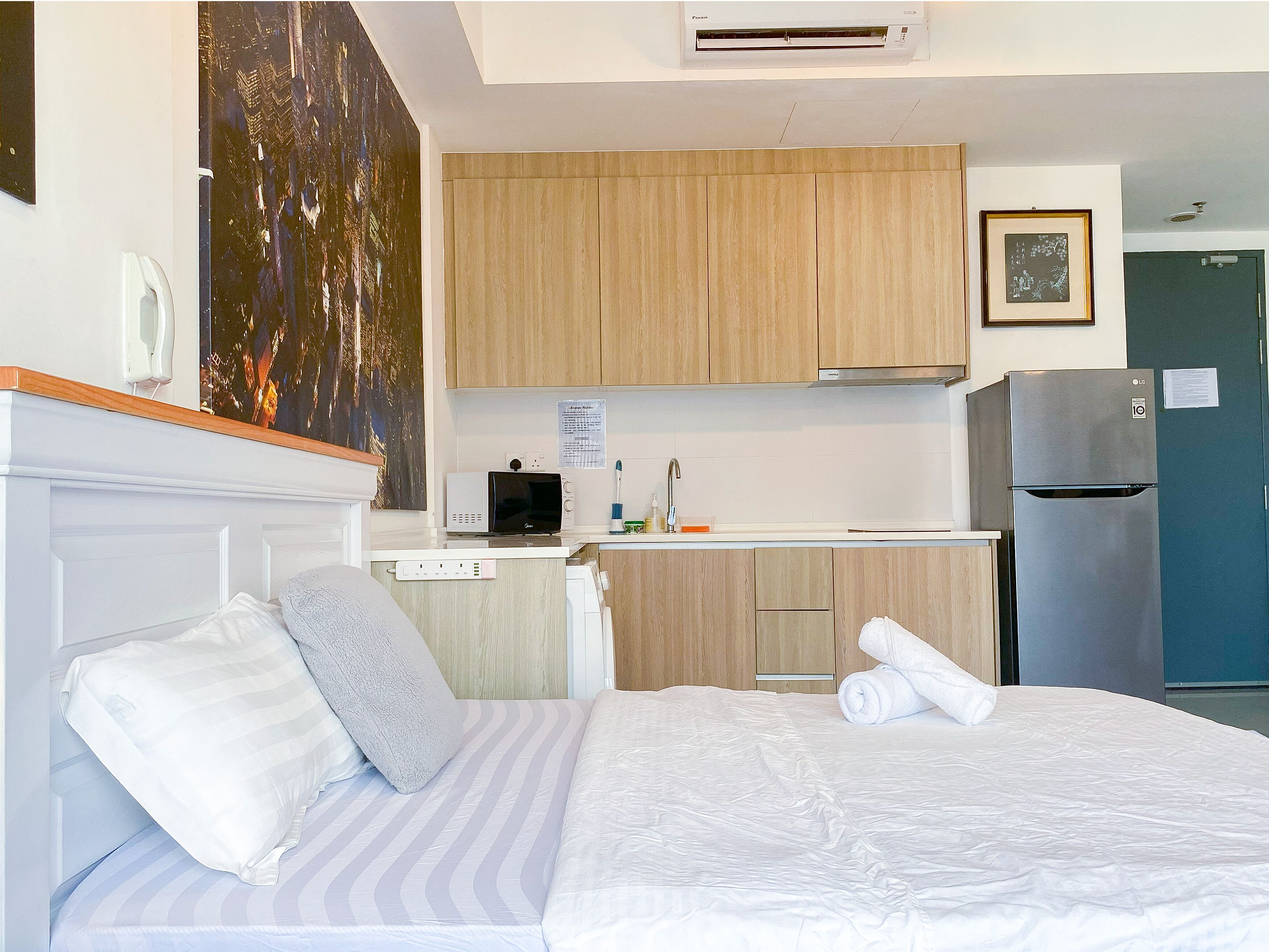 Habitación de hotel con cama, kitchenette, microondas, refrigerador y un cuadro en la pared.