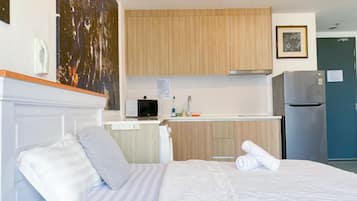 A hotel room with a bed, a small kitchenette, a microwave, a refrigerator, and a painting on the wall.