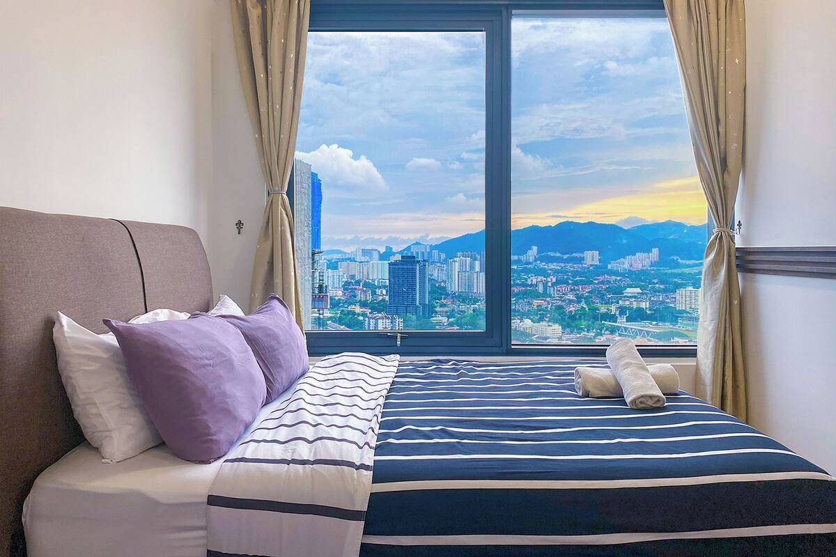 A hotel room with a bed, a view of a cityscape through a large window, and a sofa.