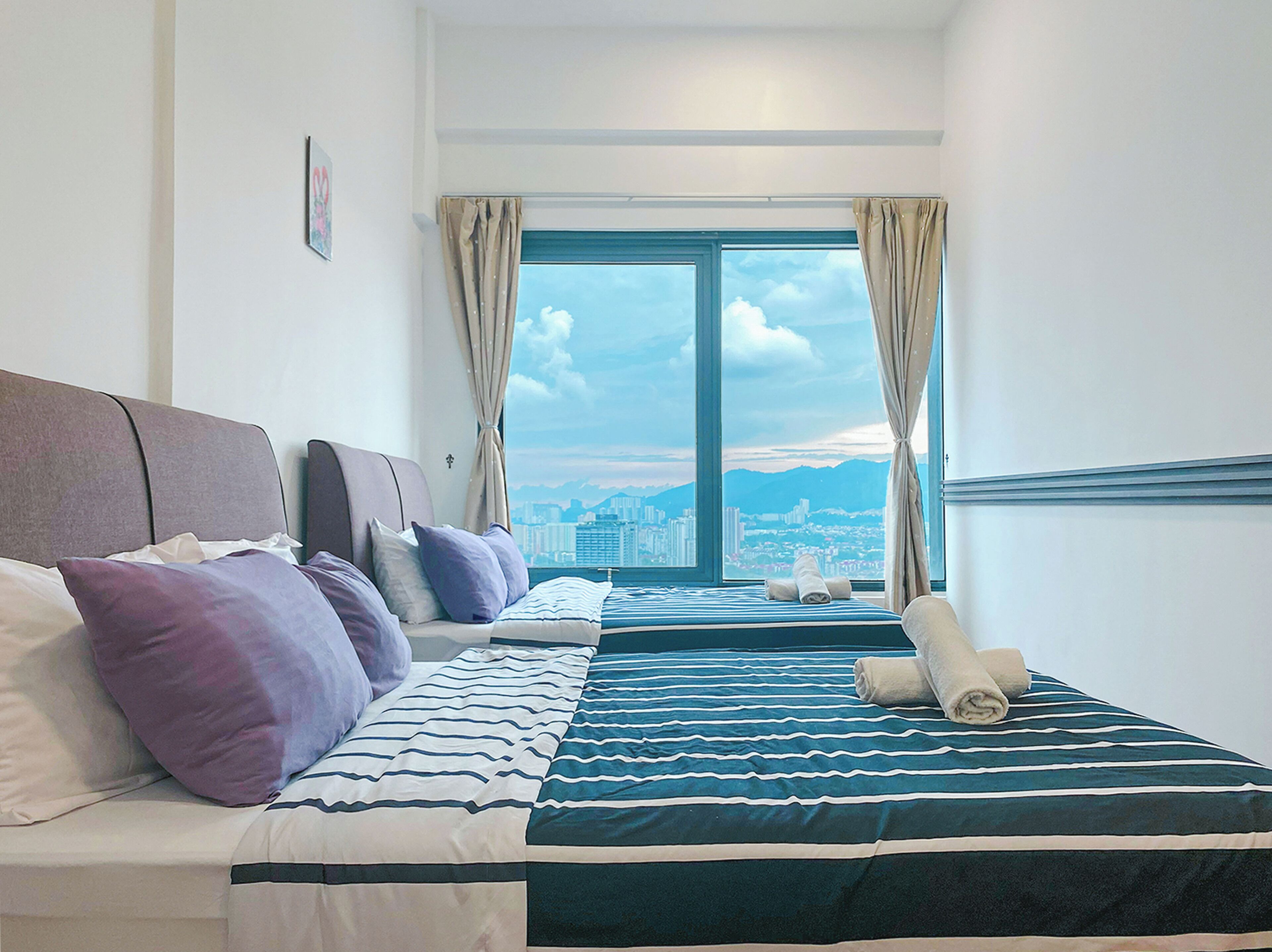 Ein Hotelzimmer mit einem großen Bett, einem kleineren Bett und Blick auf die Stadt durch das Fenster.
