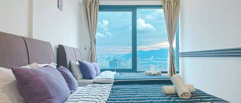 A hotel room with a large bed, a smaller bed, and a view of the cityscape through the window.