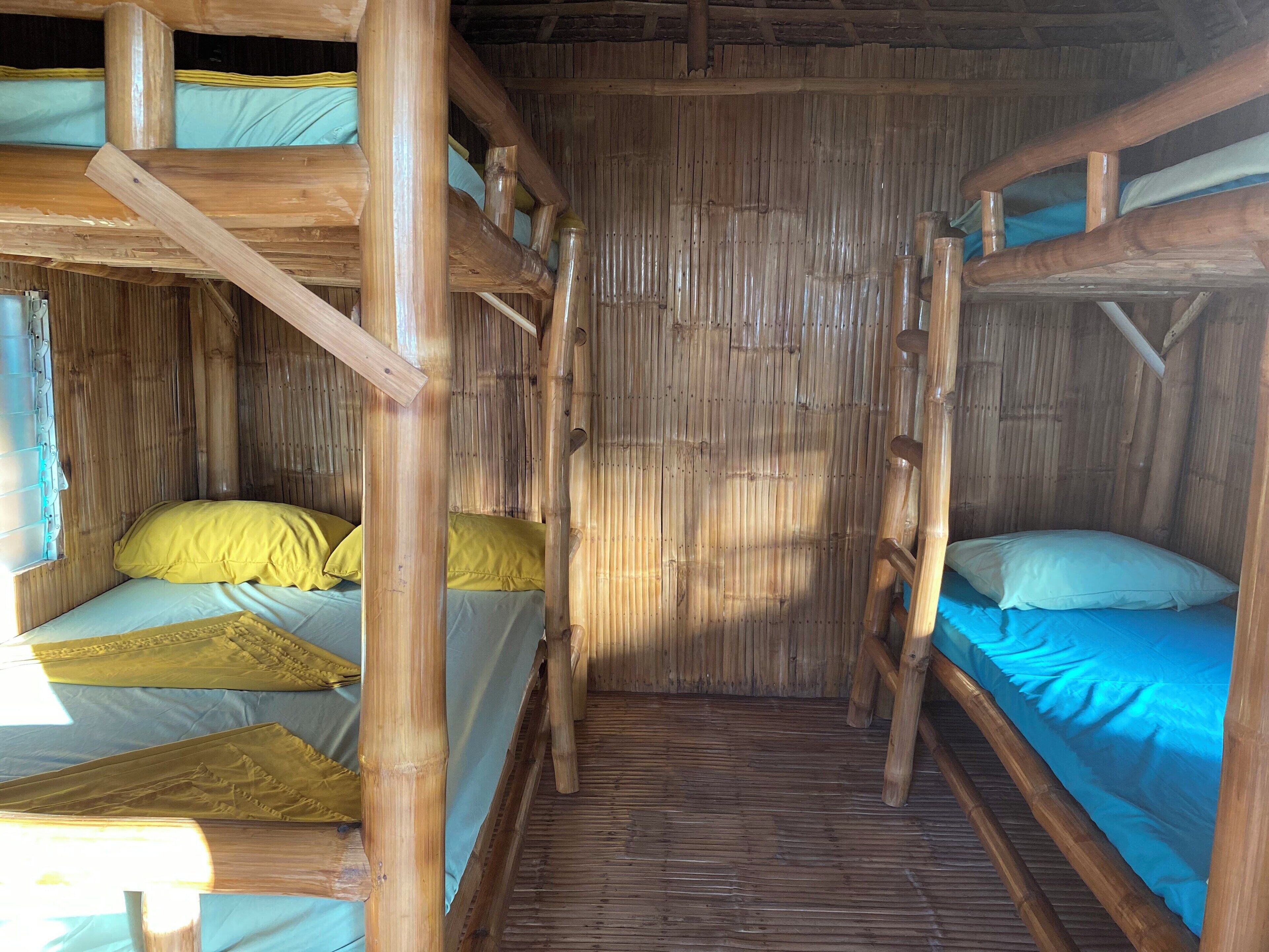 A rustic wooden room with bunk beds, bamboo walls, and a sloped ceiling.