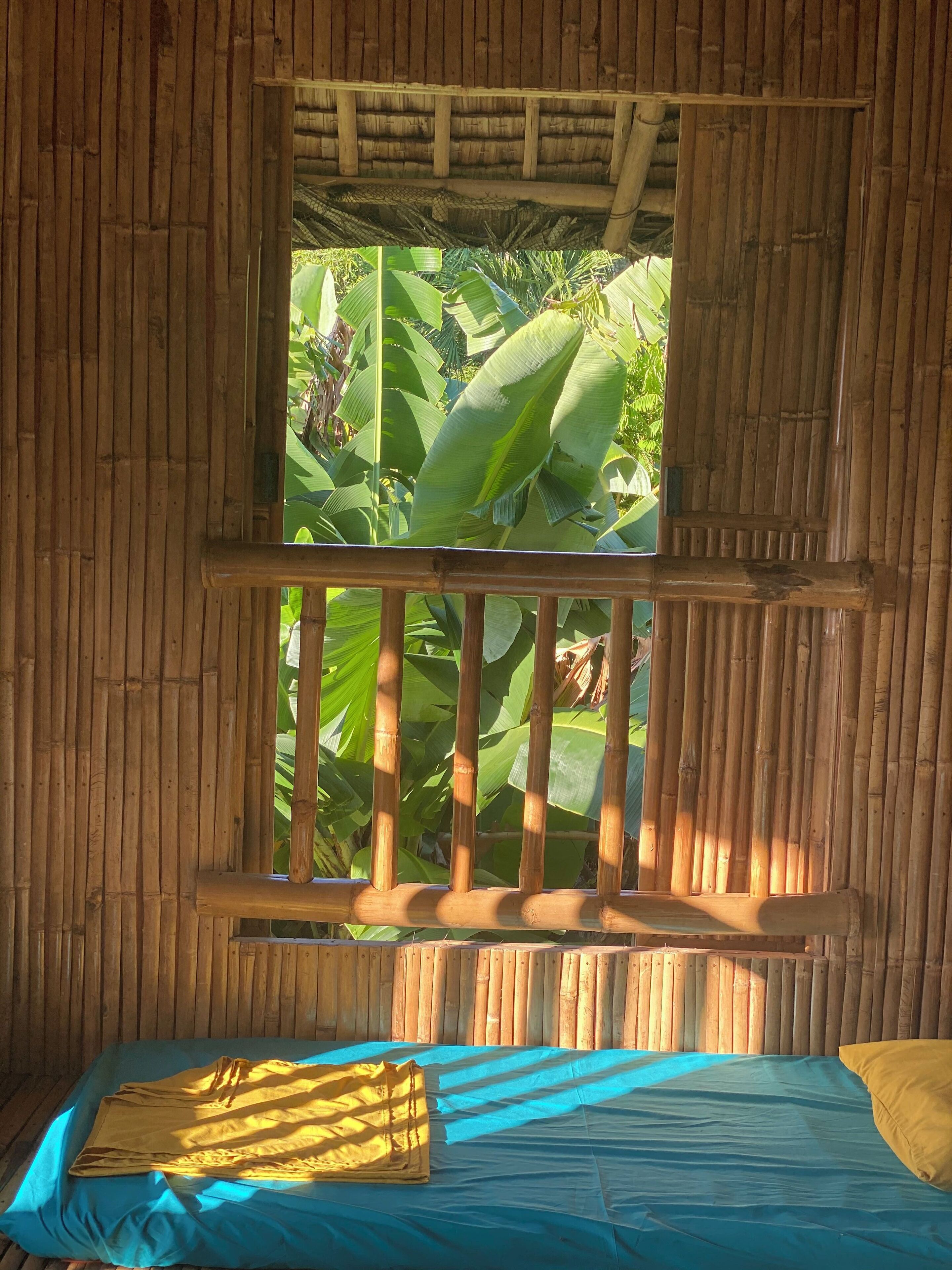 A room with a bed, a window with a wooden frame, and a view of greenery outside.