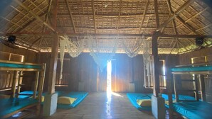 A room with a thatched roof, bamboo flooring, and multiple bunk beds with blue bedding. - Rustique Rue (Mabini)
