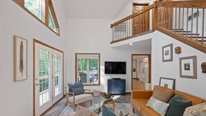 A spacious living area with a high ceiling, a wooden staircase, and a television mounted on the wall. - Fels Haus- Hot Tub, WiFi, Gas Grill, located on Cliffview Resort (Campton)
