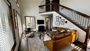 A spacious living room with a high ceiling, a staircase, and a fireplace. - Fels Haus- Hot Tub, WiFi, Gas Grill, located on Cliffview Resort (Campton)