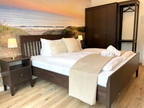 Ein Schlafzimmer mit Bett, Nachttischen, einem Kleiderschrank und einem Wandbild mit Strandmotiv.