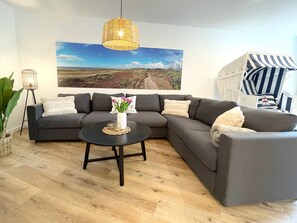 Ein modernes Wohnzimmer mit einem Ecksofa, einem runden Couchtisch, einer Korbtropflicht, einem großen Landschaftsbild und einem gestreiften Sessel.