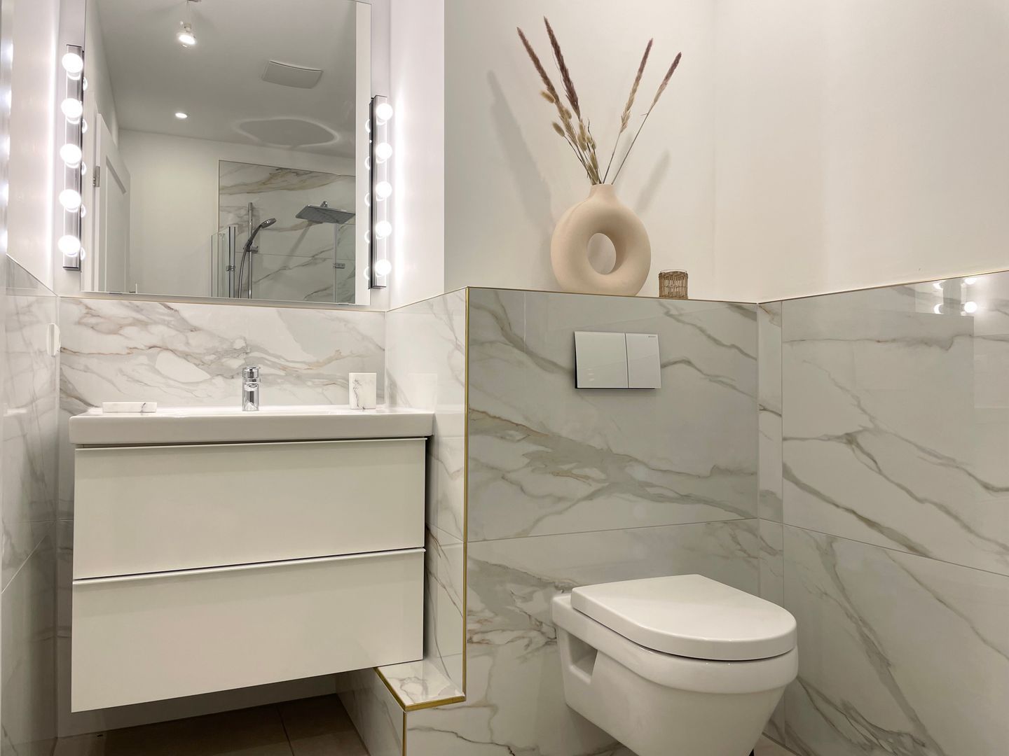Une salle de bain moderne avec un meuble-lavabo en marbre, des toilettes et un miroir avec éclairage intégré.