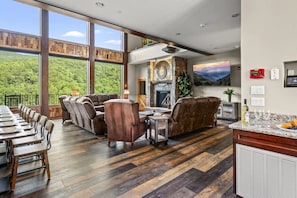 A spacious living area with a fireplace, large windows, and a dining area with a long table and chairs.