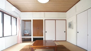 Una habitación tradicional japonesa con suelo de tatami, una mesa de madera, puertas correderas y un televisor sobre un soporte.