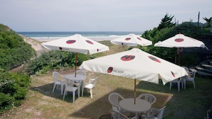 Un área de estar al aire libre frente al mar, con sombrillas blancas y sillas de plástico.