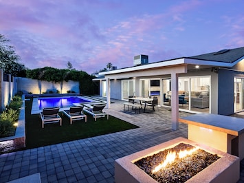 Beautiful backyard featuring a sparkling pool, a patio with an outdoor dining area, tanning chairs, a fire place, and a grill area.