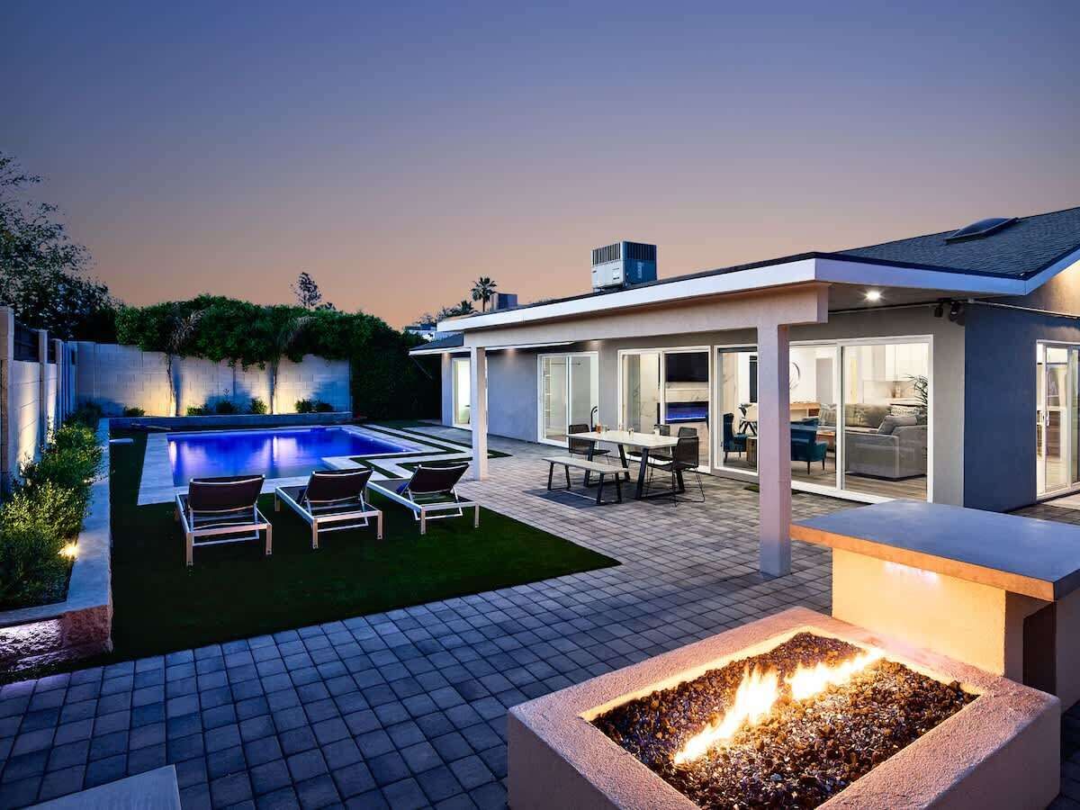 Beautiful backyard featuring a sparkling pool, a patio with an outdoor dining area, tanning chairs, a fire place, and a grill area.