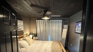 Ein gemütliches, helles Schlafzimmer mit Holzboden, einem Einzelbett mit weißer Bettwäsche, einem Nachttisch und einem kleinen Tisch.