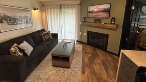 Ein Wohnzimmer mit einem dunklen Sofa, einem Couchtisch, einem Kamin und einem großen, gerahmten Bild an der Wand.