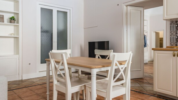 Un coin repas avec une table en bois et des chaises blanches, un meuble blanc et un sol carrelé.