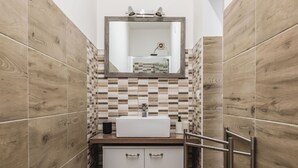 Une salle de bain avec un plancher en bois, un lavabo blanc, un miroir et un mur recouvert de carreaux.