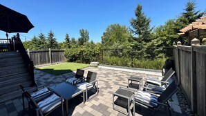 Eine Terrasse mit Gartenmöbeln, ein Holzdeck und ein von Bäumen gesäumter, umzäunter Garten.