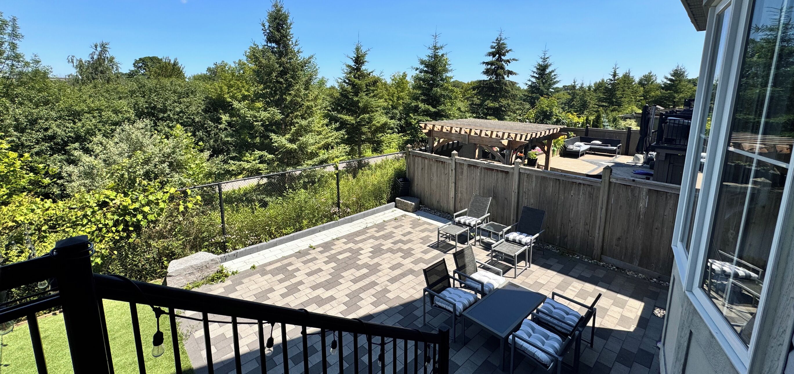 Un patio con mobiliario exterior, una pérgola y vistas a un área boscosa.