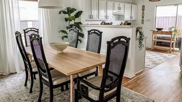 A dining area with a wooden table and four chairs, a rug, and a kitchen in the background.