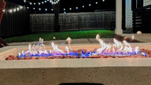 Ein Feuerstelle mit freier Sicht auf die Flammen und einem Holzzaun im Hintergrund.