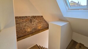 Een loft-achtige kamer met een zichtbare bakstenen muur, een schuine plafond en dakraam.