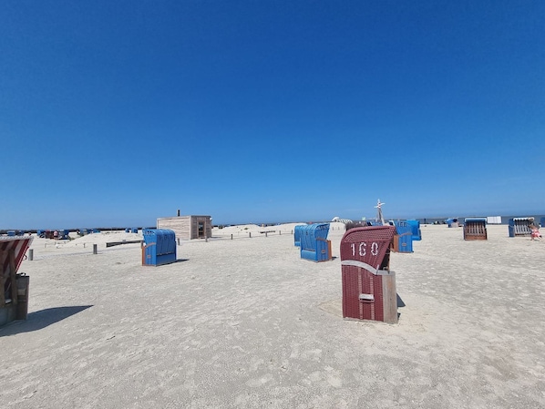 A beach with blue and red beach chairs, a small wooden structure, and a lifeguard tower.