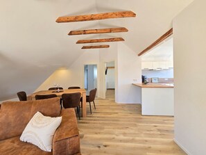 A modern loft with a dining area, kitchen, and a cozy seating area with a brown leather couch and a white throw pillow.