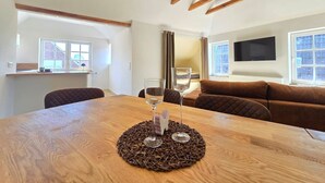 Een modern interieur met een houten eettafel, een bruine bank en een aan de muur bevestigde televisie.