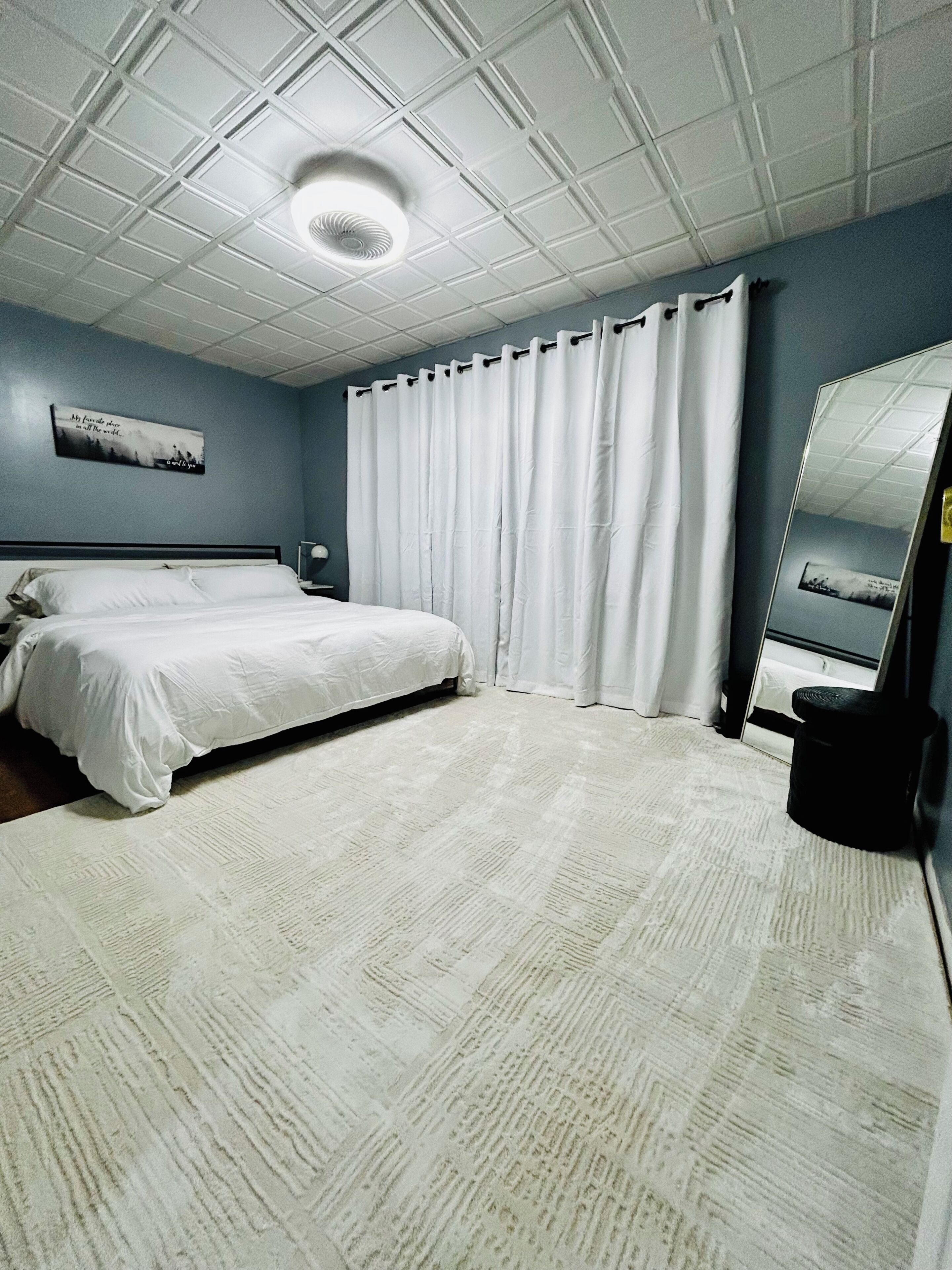Une chambre d’hôtel avec un grand lit, une table de chevet, un miroir et un ventilateur de plafond.