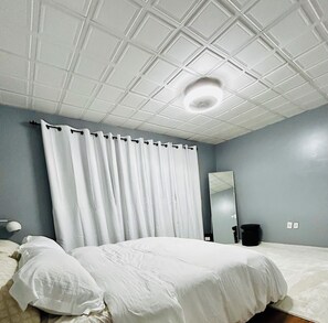 A bedroom with a single bed, a ceiling fan, a mirror, and a nightstand.