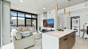 A modern kitchen with a central island, a dining area with a sofa and coffee table, and a large window offering a view of the outdoors. - 2bd/2ba Best style and location/Pool+spa/gym/pkg! (Salt Lake City)
