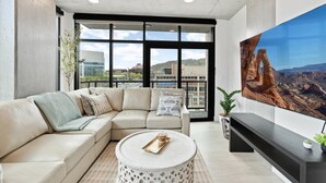 A modern living room with a beige sectional sofa, a round coffee table, and a large flat-screen TV mounted on the wall. - 2bd/2ba Best style and location/Pool+spa/gym/pkg! (Salt Lake City)