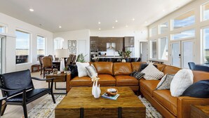 Uma sala de estar ampla, com sofá de couro, mesa de centro e área de refeições com cadeiras e mesa.