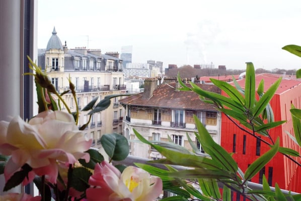 A view from a window overlooking a cityscape with buildings of varying architectural styles, including a red building with vertical windows.